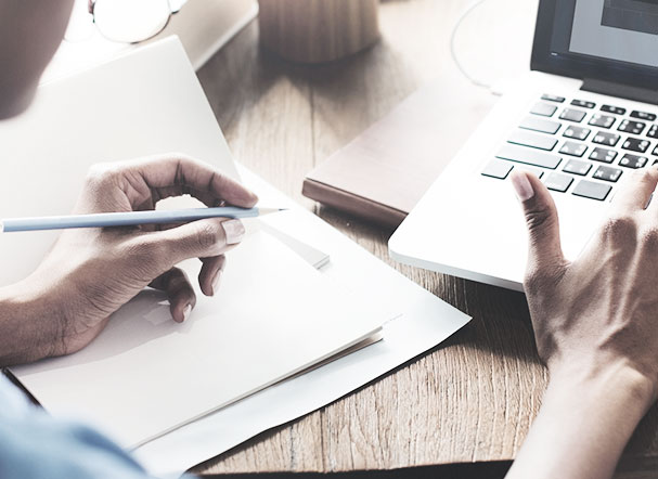 Person typing on notebook with right hand and writing on paper with left hand