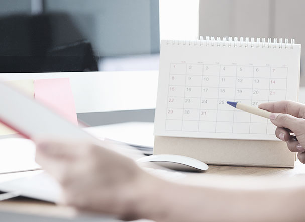 Pessoa verificando calendário enquanto faz anotações em bloco de notas